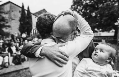 Photo émotion pendant une cérémonie de mariage, un pap tient son enfant dans les bras et serre dans ses bras son témoin, prise par le photographe de mariage en Savoie Thomas Vigliano